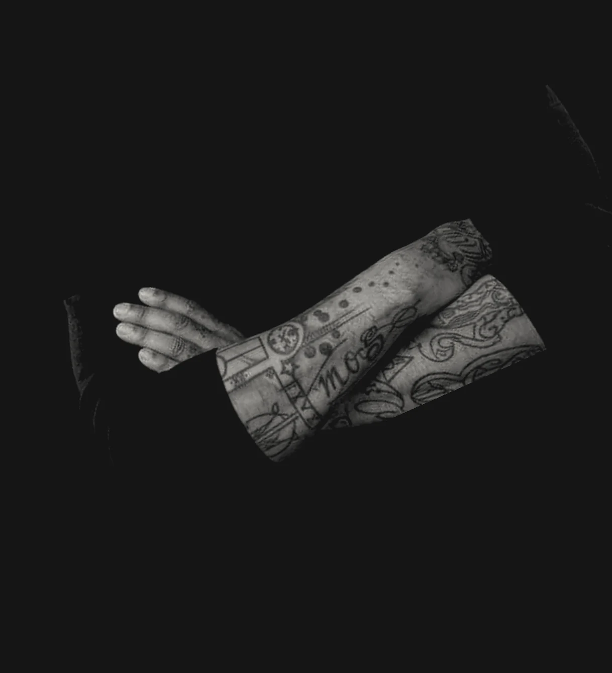 Cosmos Lemos's tattooed forearms, folded, against a black background.